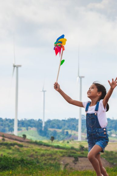 Cute asian child girl is running and playing with wind turbine t Cute asian child girl is running and playing with wind turbine toy with fun in the wind turbine field